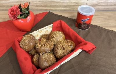 Fotografia de pãezinhos de nescau com castanhas dentro de uma cestinha branca quadrada com um pano vermelho. A cestinha está sobre um pano marrom de tom escuro, ao lado da latia de nescau extra cacau. Fotografia de pãezinhos de nescau com castanhas dentro de uma cestinha branca quadrada com um pano vermelho. A cestinha está sobre um pano marrom de tom escuro, ao lado da latia de nescau extra cacau.